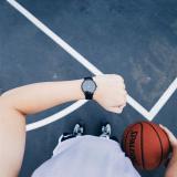 Trainer, der die schwarze runde analoge Uhr am linken Handgelenk trägt, während Basketball auf der rechten Hand ist